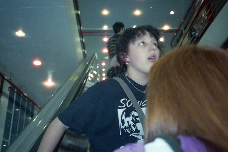 A photograph capturing a person on a train platform. The individual is looking upwards and appears surprised or curious. They are standing near a meta