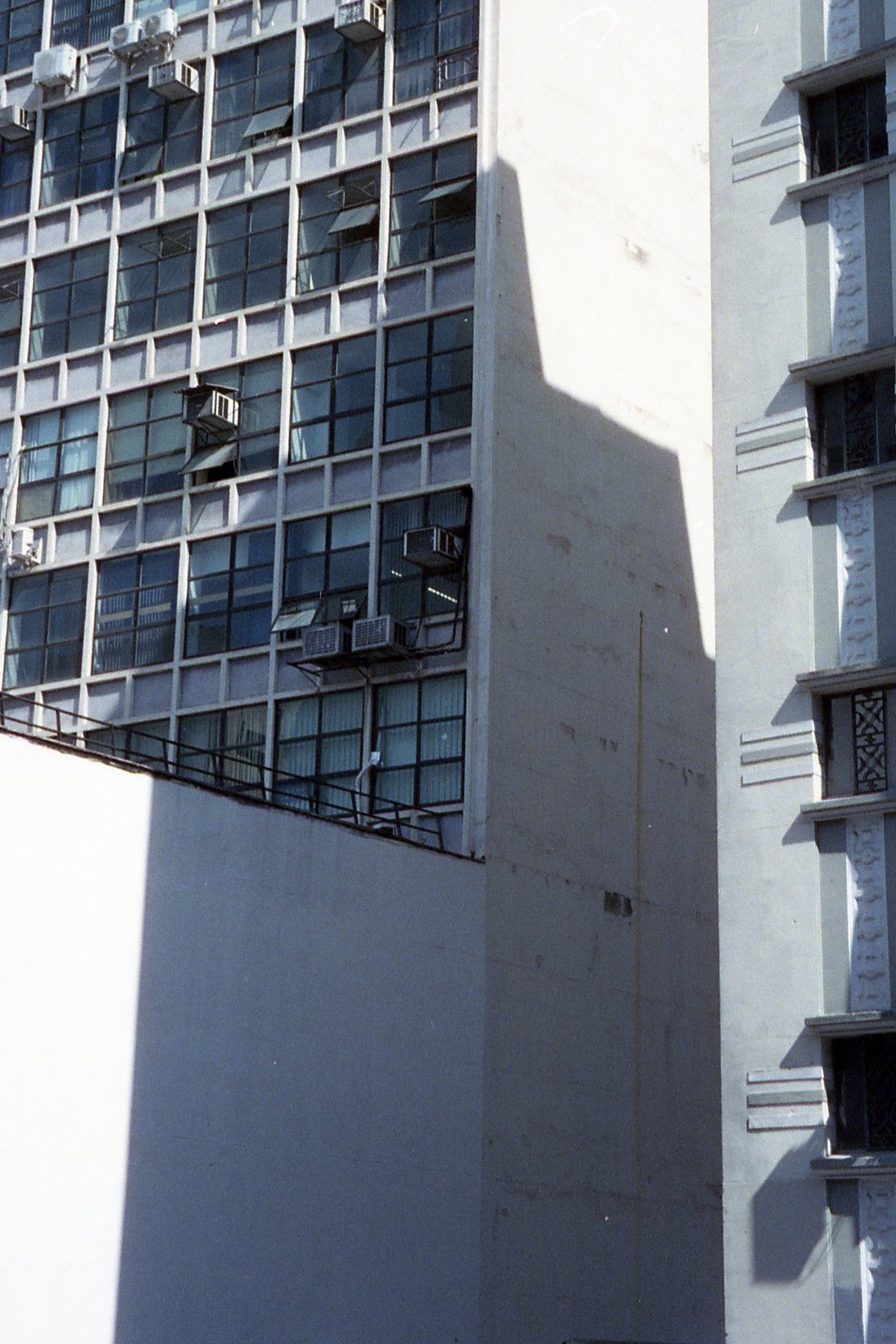 The photo shows a tall residential building. It has a prominent corner balcony on the ground floor with visible air conditioning units. The building's