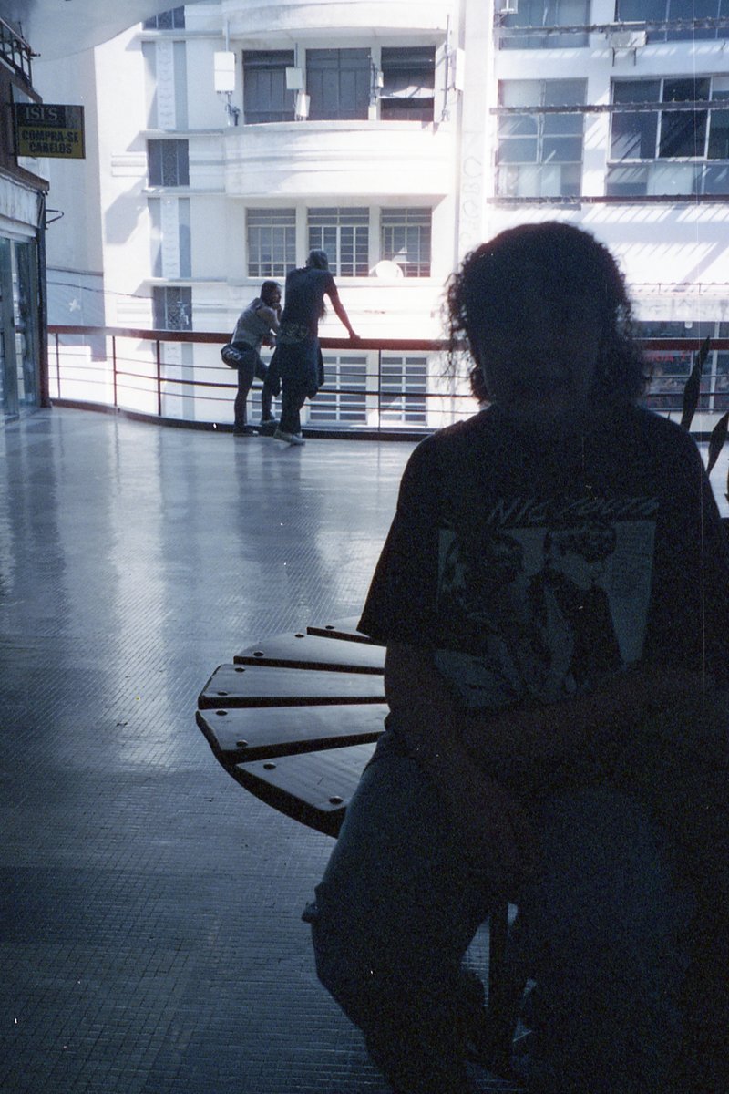 This image shows a person sitting on a bench in what appears to be a public indoor space. The individual is wearing a t-shirt with some graphic design