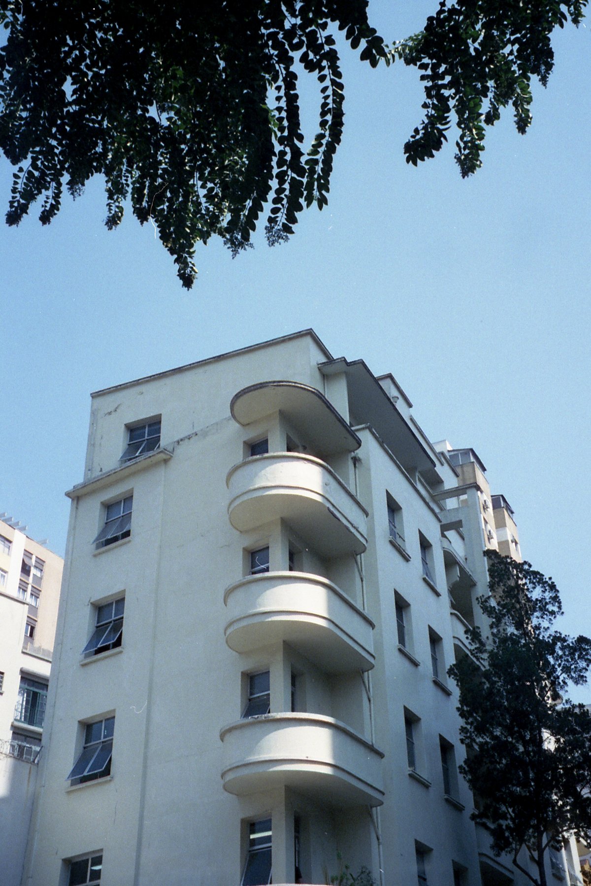 This image features a tall building with balconies, set against a clear sky. The architecture suggests a residential structure, possibly located in a 