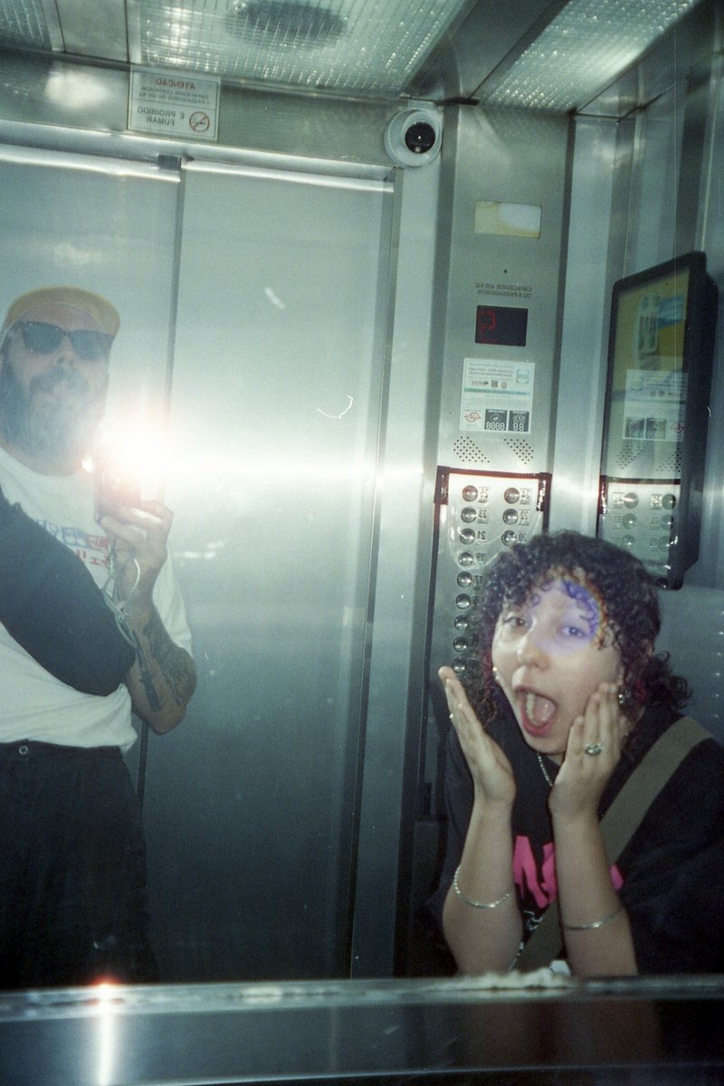 A black and white photo capturing a moment of surprise. The focus is on a woman making a shocked face, her mouth wide open. In the foreground, a man h