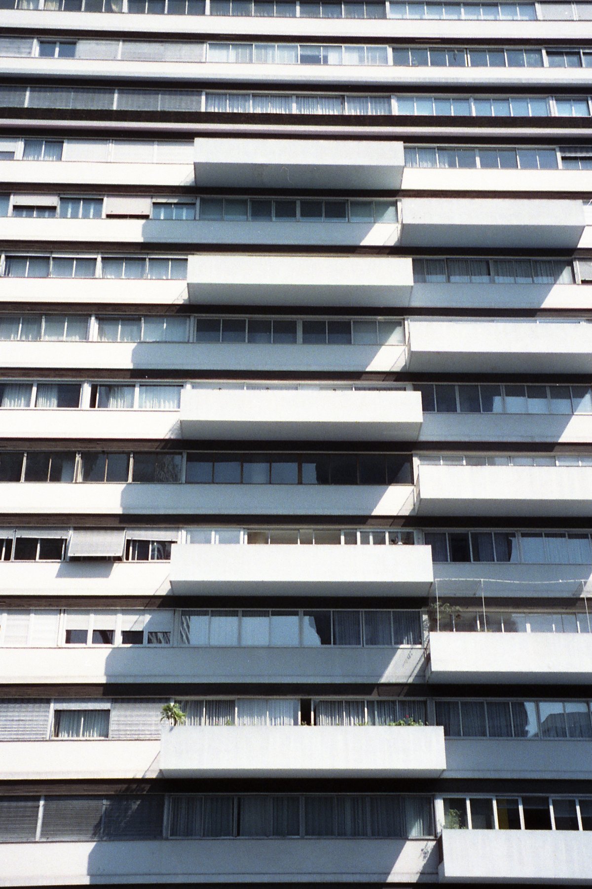 The image depicts a large building with many balconies. It appears to be constructed from concrete or stone blocks, and the balconies have railings al