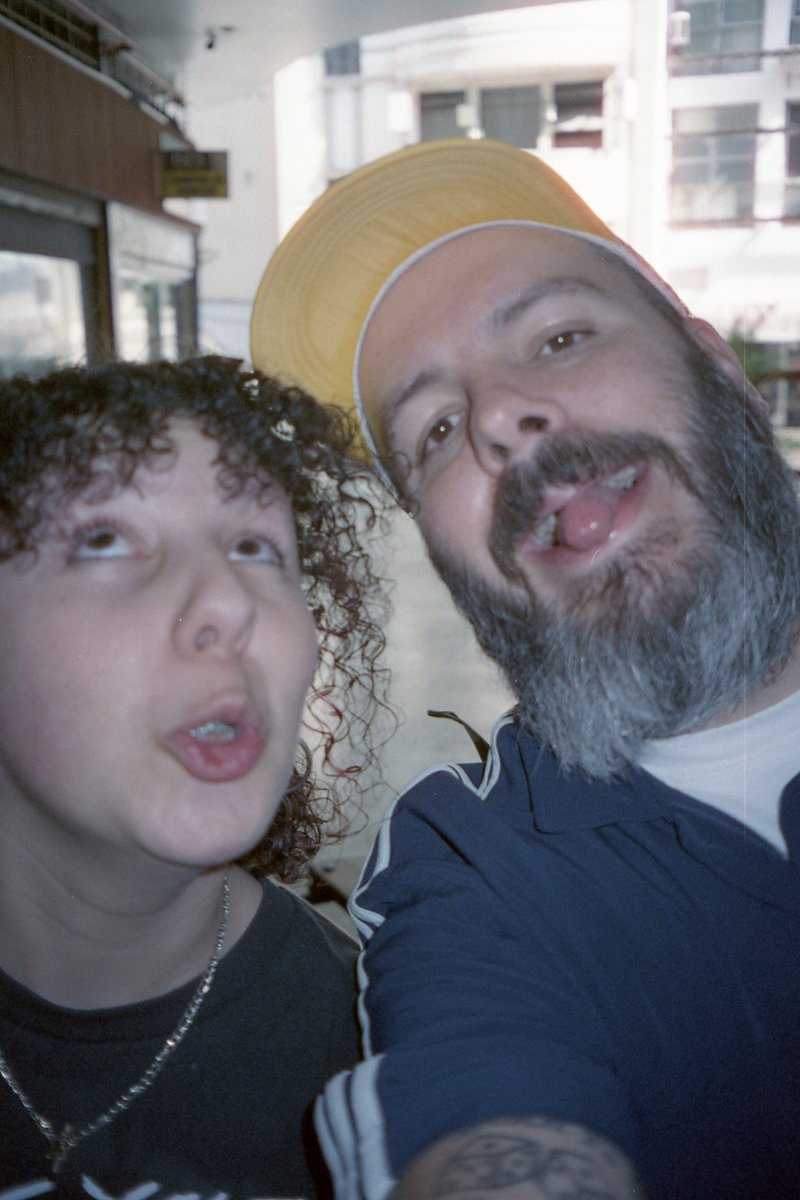 This image captures a candid moment between two men. One man is making a playful face, his tongue sticking out in an exaggerated manner. He's wearing 