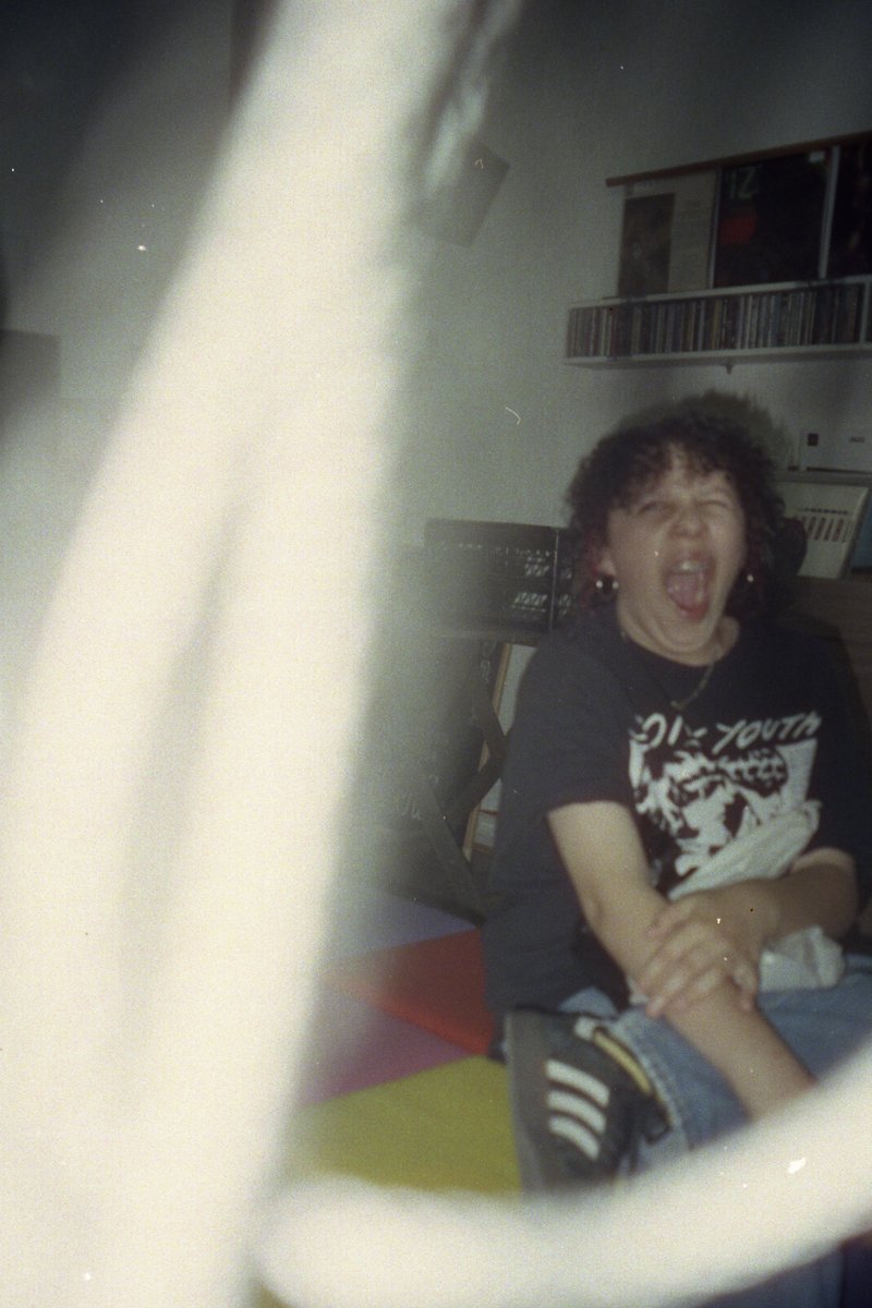 The image portrays a young man sitting on a bed. He is captured mid-yawn, adding a sense of dynamism to the scene. His attire consists of a black t-sh