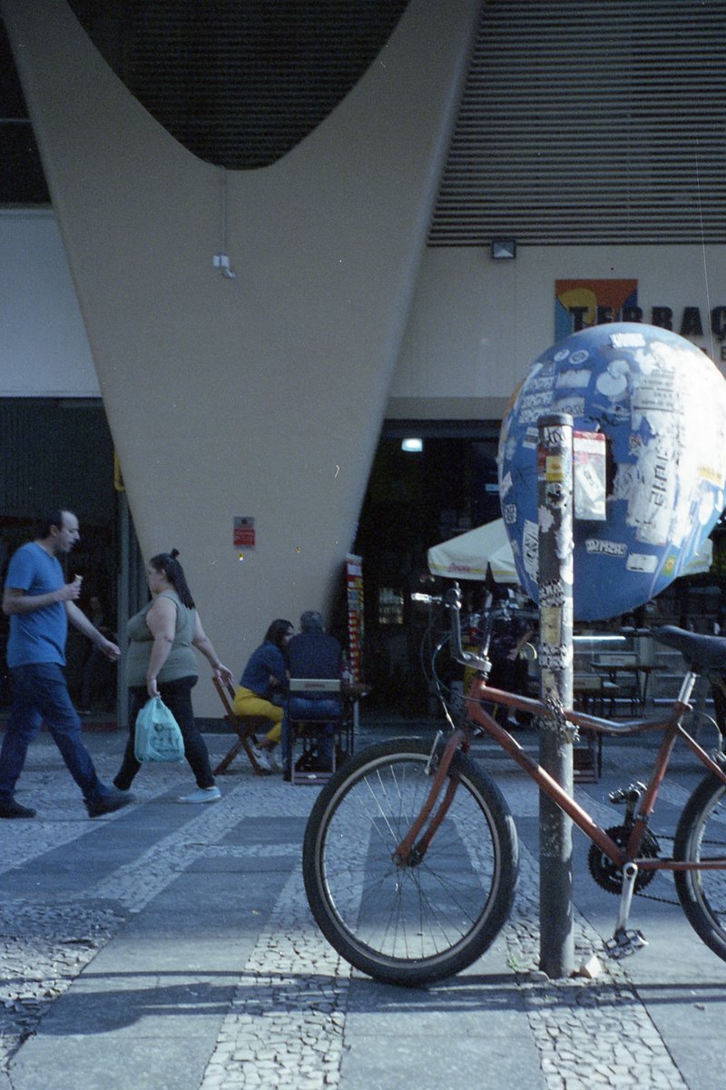 The image is a photograph of an outdoor urban setting. It features a bicycle parked on the sidewalk alongside a bike rack. In front of the bicycle and