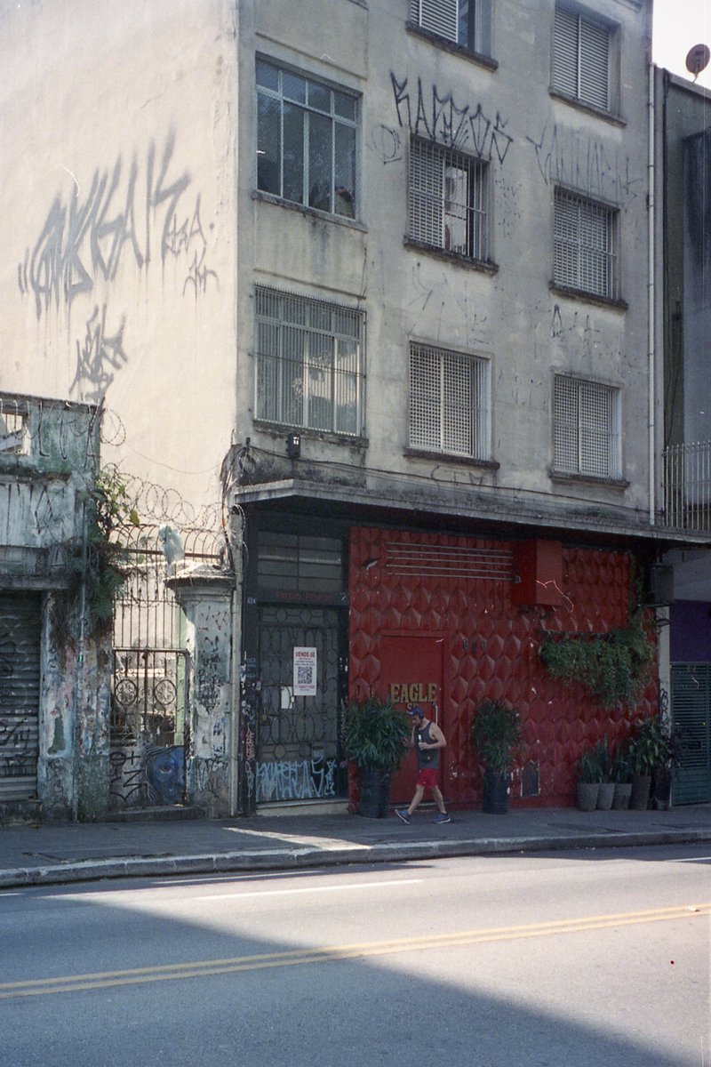 The photo shows an urban scene with a graffiti-covered building in the foreground. On its facade, there's a red door with the word "SECURITY" written 