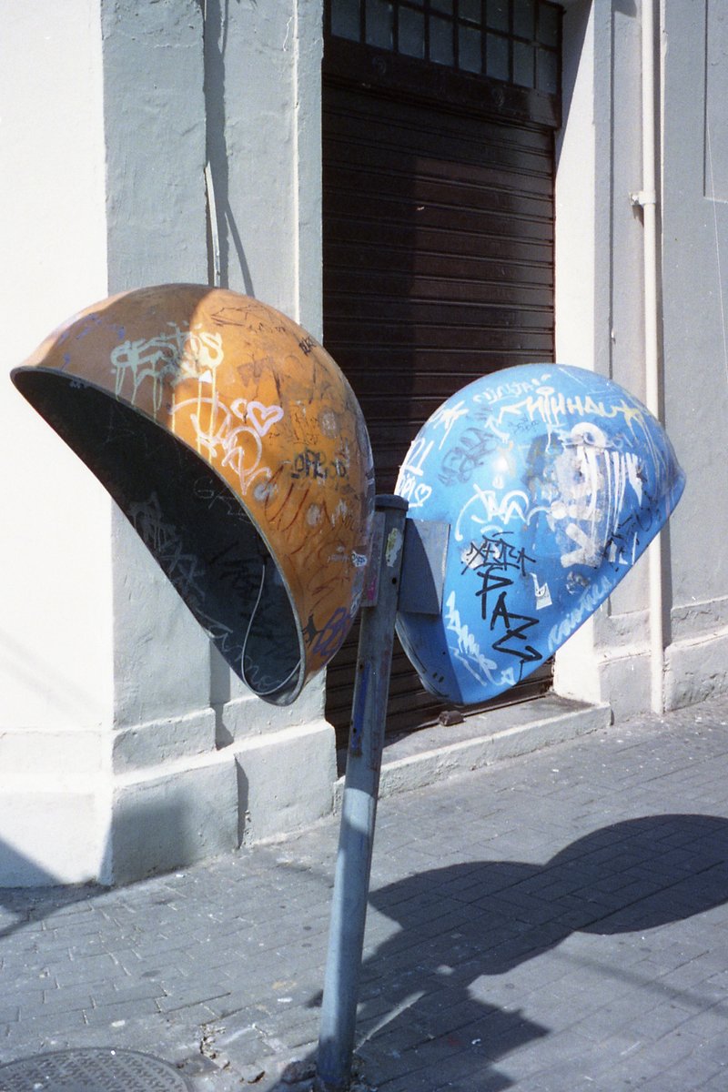 A colorful mural on the side of a building. Two mailboxes are in front, with one being blue and orange and the other green and black. They sit near a 