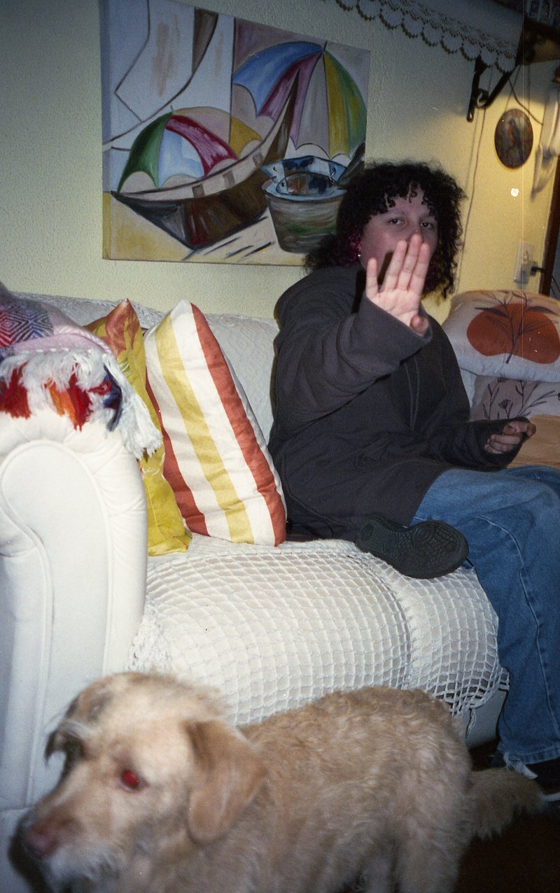 In the image, there's a person sitting on a couch, holding their hand up to their face, possibly communicating. To the right of the person is a tan do