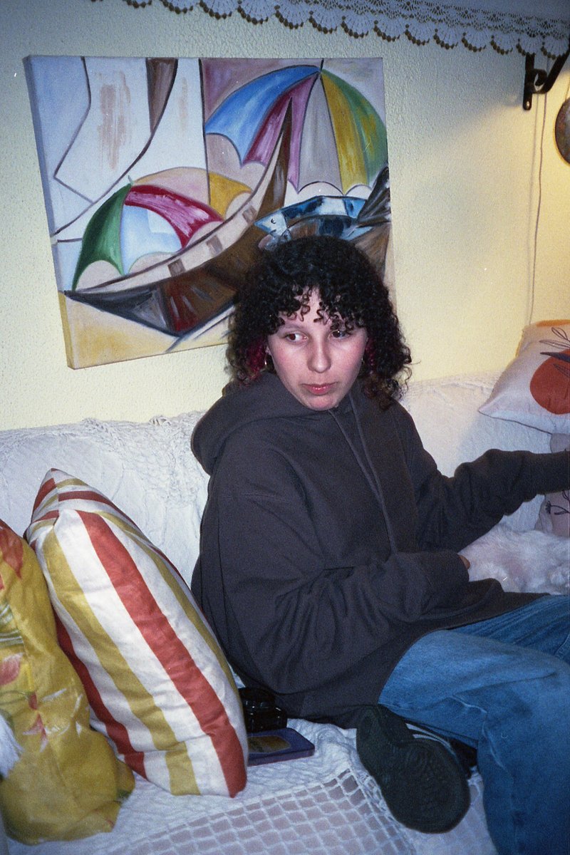 A man sits on a couch, engrossed in playing a video game. He is comfortably dressed in a casual sweatshirt and jeans. The room around him is warmly li