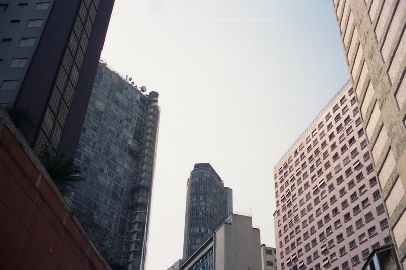 The image presents a city scene from a low angle. In the foreground, there is a red brick wall. The middle ground features multiple tall buildings wit