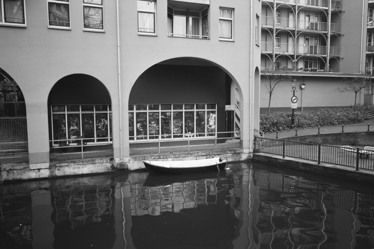  The image shows an old town scene with a boat docked near the edge of water under an archway. It seems like a rainy day as suggested by the wet street nearby. There is no text visible in the image. 