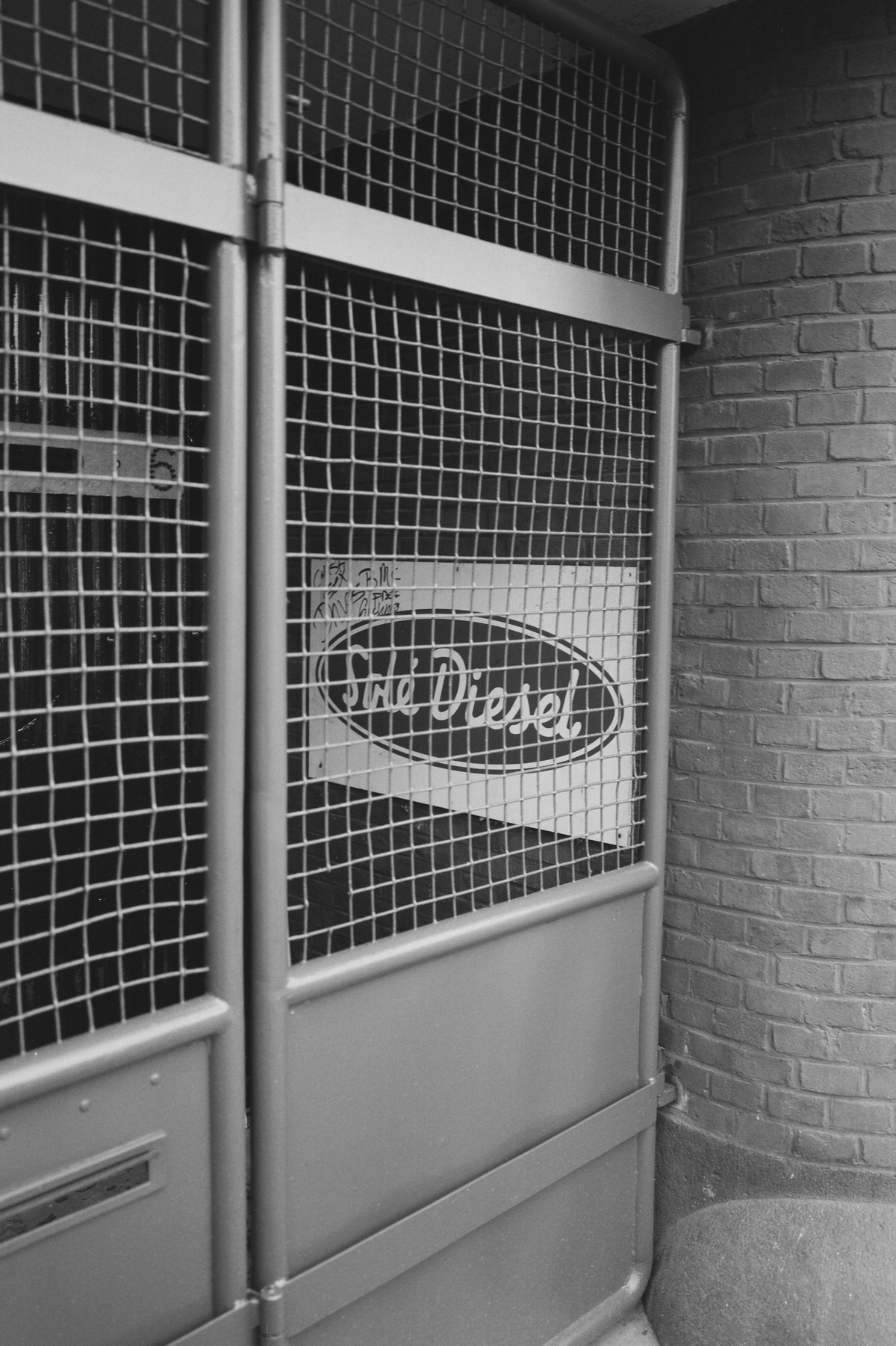  The image shows an old metal door located in what appears to be a garage or storage area. On the door is a sign with the words "THE DEPOT" visible on it, suggesting that this might be associated with a store or business named The Depot. The door has been secured with chain link fencing, indicating that access to this location may be controlled or limited. There's no indication of people or activity in the immediate vicinity of the door. 