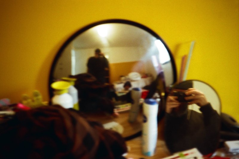 The image is split into two photos: On the left, there's a mirror reflecting a domestic scene with items scattered around, suggesting a lived-in space with some clutter; on the right, a person appears to be taking a selfie, which shows their reflection and a hand holding a smartphone.