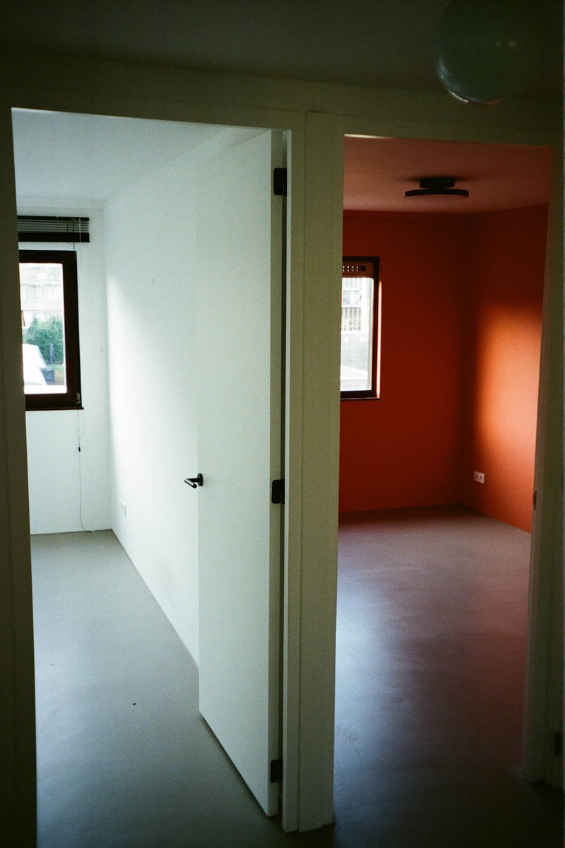 The image shows an interior view of a room, specifically focusing on two doors painted red and orange. The room appears to be an empty space with minimal decoration, featuring simple wall colors and plain flooring. There are no visible texts or distinctive features that provide additional context about the location or setting.