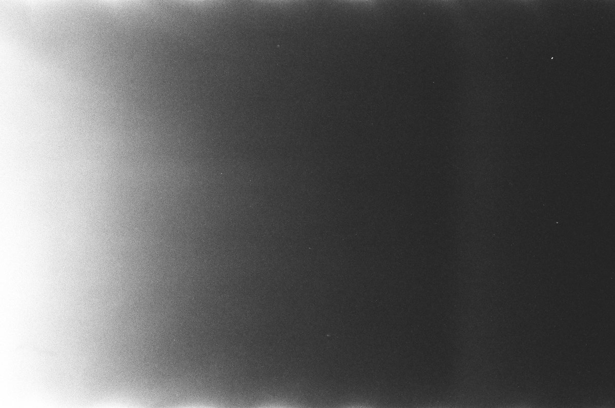  The image shows a monochromatic photograph with a blurred, high contrast quality. It appears to be a close-up of textured fabric or paper, possibly with a pattern or design that is not distinct due to the focus on the central black area. This dark void creates an optical illusion known as the "Mach bands," where the human visual system perceives an image as being lighter at the edges and darker in the center, causing the peripheral areas to seem brighter relative to the center. 