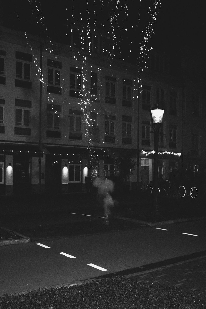 This is a nighttime photo of a city scene. Fireworks are bursting in the air, creating bright streaks against the dark sky. Below them, there's a buil