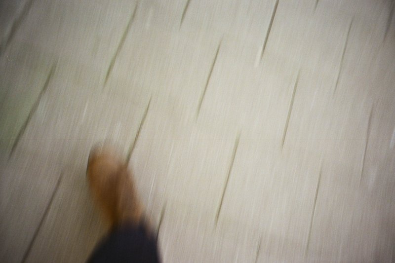 The image depicts a blurred photograph of a person walking away from the camera, down an alley or hallway lined with bricks. The flooring is also brick patterned, suggesting a pedestrian walkway. Due to the blurriness and low resolution, no other details can be confidently described.