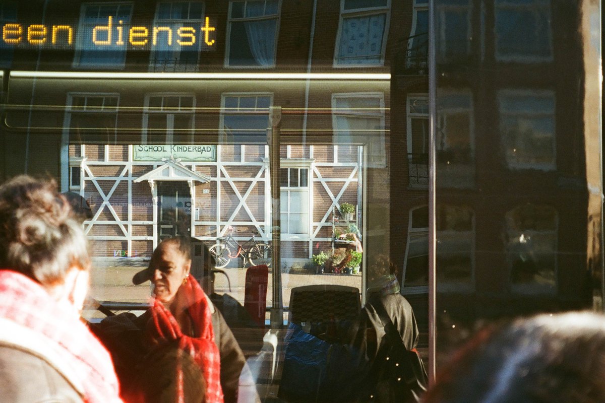  The image shows a scene from a busy street with people walking by. There's a storefront displaying various items, possibly merchandise or decorations. An individual is taking a photo of the scene outside through the shop window. The weather appears to be overcast, suggesting it might be raining or about to rain. 