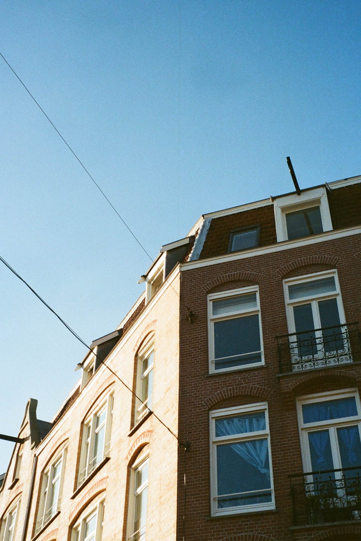  The image shows a residential building with multiple windows, situated under an overcast sky. There is no visible text within the image that provides additional context. The building appears to be constructed from brick and has a balcony on one of its levels. In the foreground, there is a clear view of a streetlight, which extends vertically across the frame. The style of the photograph suggests it was taken during the daytime under natural light conditions. There are no people or distinctive objects that would indicate specific activities taking place in the scene. 